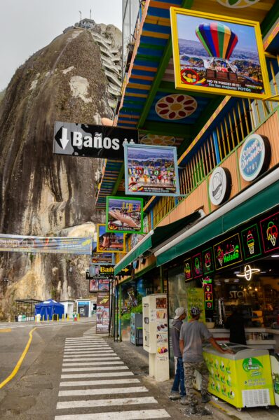 Colorful shops and signs line the street at Guatapé, Colombia, with the towering El Peñol rock in the background.