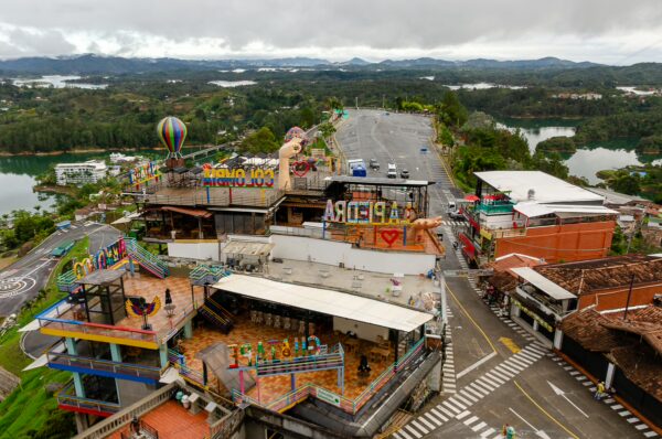 Colorful rooftops and vibrant decorations overlook the lush landscape of Guatapé, Antioquia, with distant mountains and lakes visible.