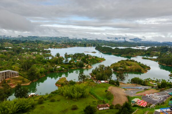 Panoramic view of lush green hills and lakes surrounding El Peñol Rock in Guatapé, Antioquia, Colombia under a cloudy sky.