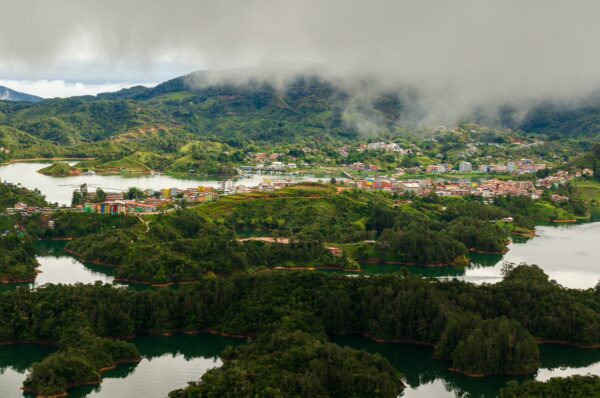 Stunning aerial view of Guatapé, Antioquia, Colombia, showcasing lush green hills, tranquil lakes, and colorful buildings under a cloudy sky.