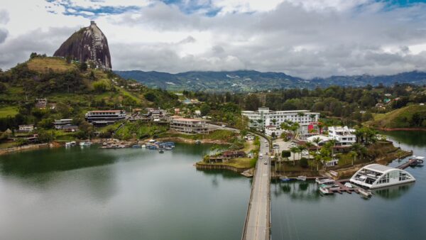 El Peñol Rock towers over the scenic lake in Guatapé, Antioquia, Colombia, surrounded by lush green hills and vibrant buildings.