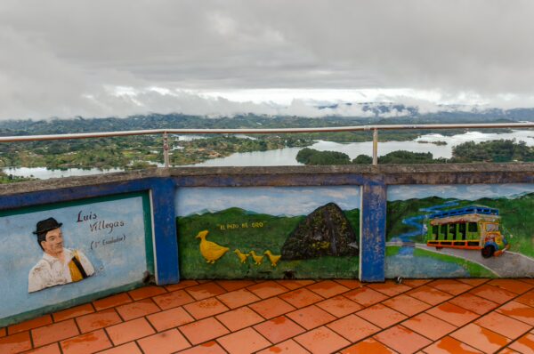 View from El Peñol rock in Guatapé, Antioquia, Colombia, showcasing colorful murals and a cloudy landscape with lakes in the background.