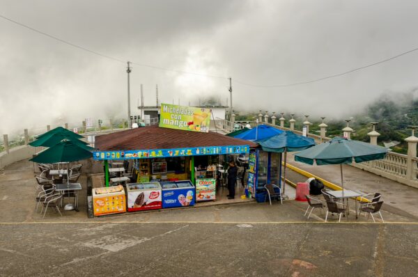 Colorful food stall with umbrellas at El Peñol Rock in Guatapé, Antioquia, surrounded by misty clouds and scenic views.