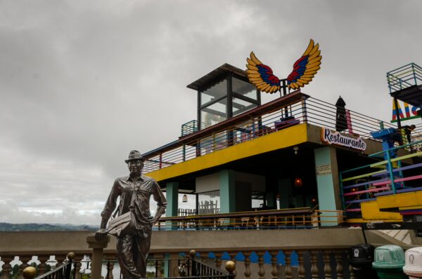 El Peñol, Guatapé, Antioquia, Colombia: Colorful waterfront café with a vibrant eagle sculpture, overlooking the lake on a cloudy day.