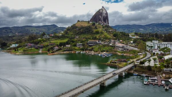 El Peñol Rock in Guatapé, Antioquia, Colombia, towers over the emerald lake, surrounded by lush green hills and vibrant buildings.