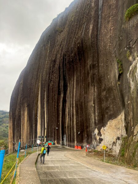El Peñol Rock in Guatapé, Antioquia features a massive, vertical rock face surrounded by a pathway and lush greenery.