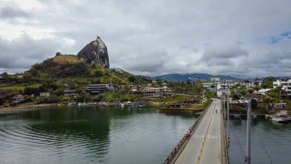 El Peñol Rock in Guatapé, Antioquia, Colombia rises prominently over calm waters, with lush greenery and charming buildings nearby.