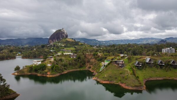 El Peñol Rock in Guatapé, Antioquia, Colombia, rises dramatically over a serene lake surrounded by lush greenery and cloudy skies.