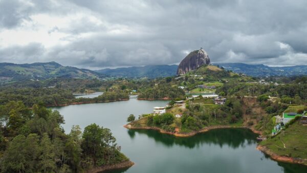 El Peñol Rock in Guatapé, Antioquia, Colombia, towers over a serene lake with lush greenery and dramatic cloudy skies.