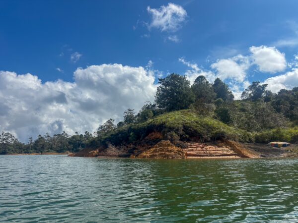 Guatapé Reservoir in Antioquia, Colombia, features lush green hills and tranquil waters under a partly cloudy sky.