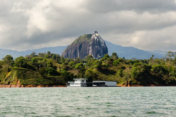 Guatapé Reservoir, Antioquia, Colombia, features lush green hills and a striking rock formation under a cloudy sky.