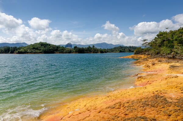 Guatapé Reservoir, Antioquia, Colombia features vibrant yellow shores, clear blue water, and lush green hills under a bright sky.