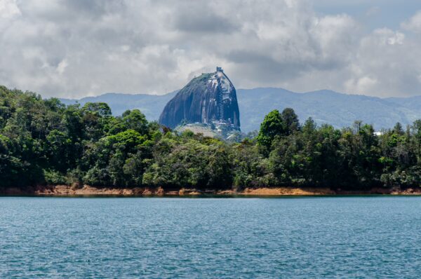 Guatapé Reservoir, Antioquia, Colombia features a lush green shoreline with a prominent rock formation rising above the water.
