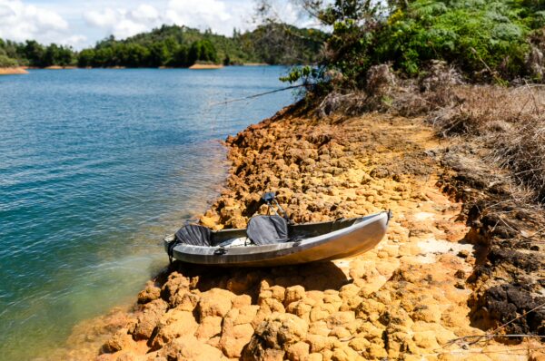 Guatapé Reservoir, Antioquia, Colombia features a tranquil blue water scene with a small boat resting on a rocky shore.