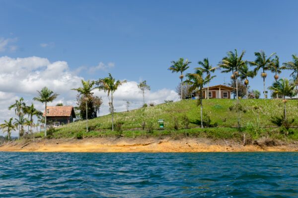 Guatapé Reservoir, Antioquia, Colombia, features lush green hills, palm trees, and a charming house overlooking the water.
