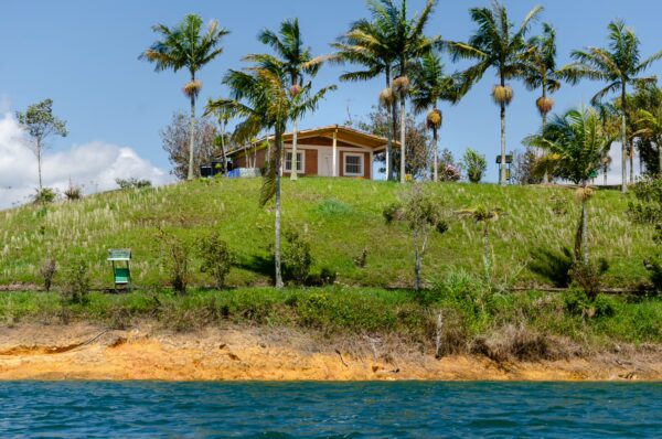 Guatape Reservoir, Antioquia, Colombia, featuring a lush hillside with a house surrounded by palm trees and a sandy shoreline.