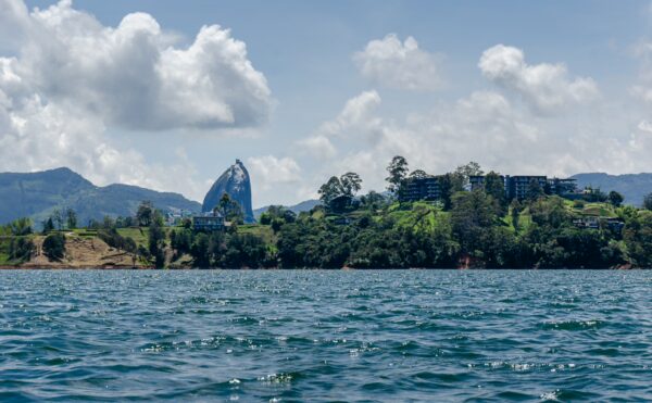 Guatapé Reservoir in Antioquia, Colombia, showcases clear blue waters, lush green hills, and a modern building against a cloudy sky.