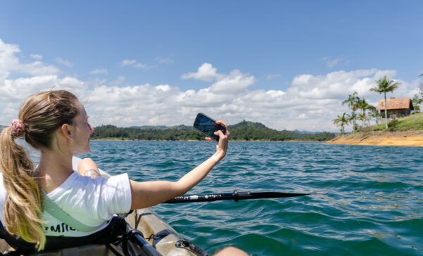 Kayaker taking a selfie on the tranquil waters of Guatapé Reservoir, surrounded by lush green hills and a bright blue sky.