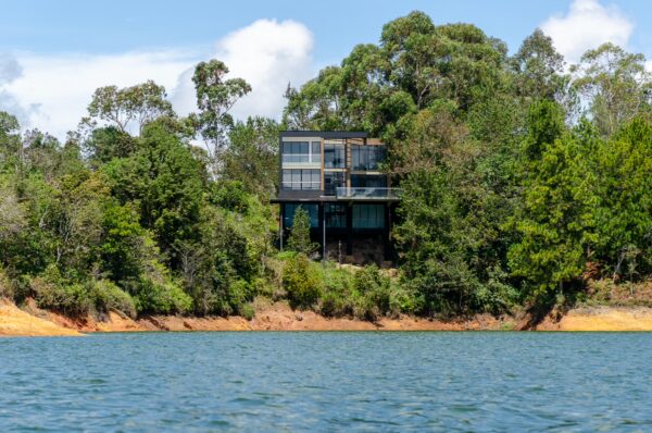 Guatapé Reservoir, Antioquia, Colombia features a modern house on a green hillside, surrounded by lush trees and clear blue water.