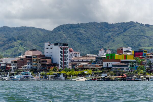 Guatapé Reservoir, Antioquia, Colombia showcases vibrant buildings along the waterfront, set against lush green mountains and a cloudy sky.