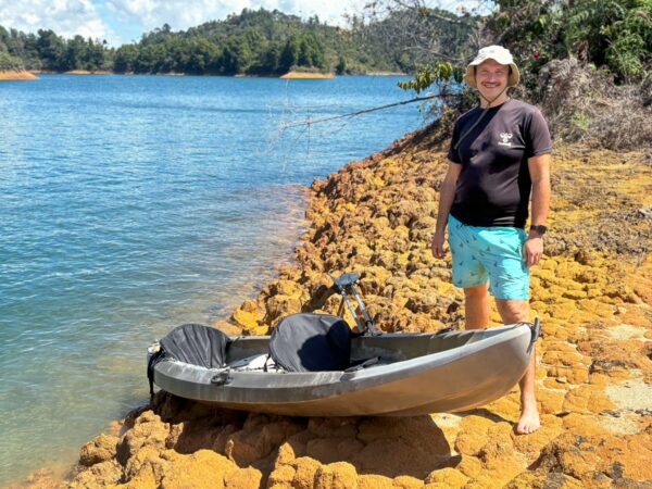 Guatapé Reservoir, Antioquia, Colombia: A person stands on a rocky shore near a kayak, with lush greenery and water in the background.