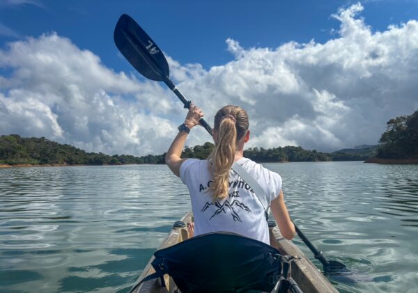 Kayaker paddling on the tranquil Guatapé Reservoir in Antioquia, Colombia, surrounded by lush greenery and blue skies.