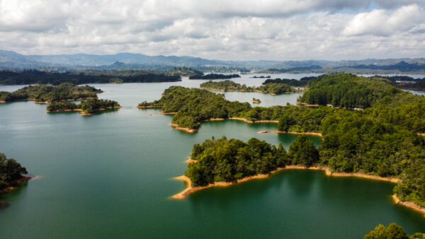 Guatapé Reservoir in Antioquia, Colombia, featuring tranquil blue waters, lush green islands, and a dramatic sky with scattered clouds.