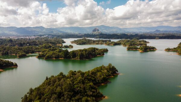 Guatapé Reservoir in Antioquia, Colombia, features emerald waters surrounded by lush green islets and a vibrant cloudy sky.