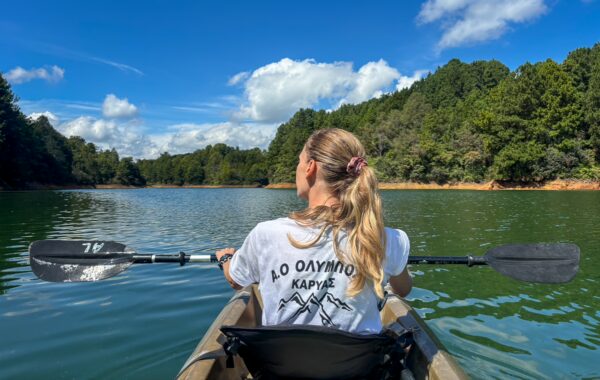 Person kayaking on the Embalse Peñol-Guatapé surrounded by forested hills under a blue sky