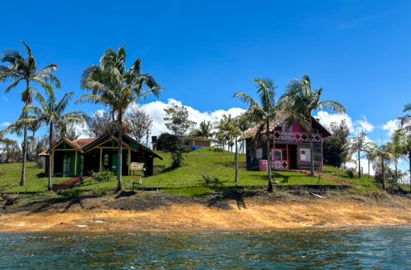Colorful houses nestled on a lush hill overlooking the Guatapé Reservoir in Antioquia, Colombia, with clear blue skies and palm trees.