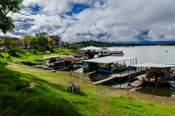 Lush green banks with boats docked by the shimmering lake, under a dramatic sky in Guatapé, Antioquia, Colombia.