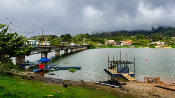 A tranquil view of Guatapé, Colombia, featuring a bridge over the lake and a small dock with boats surrounded by greenery.