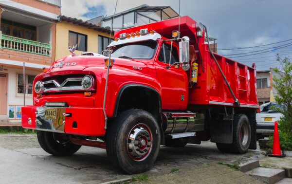 A vibrant red vintage dump truck parked on a street in Guatapé, surrounded by colorful buildings typical of Antioquia, Colombia.
