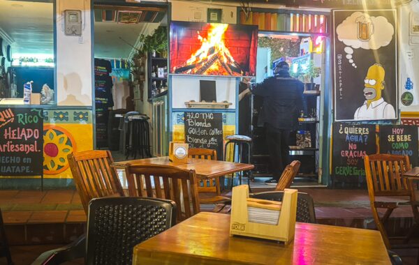 Vibrant café scene in Guatapé, featuring colorful murals, wooden tables, and a cozy atmosphere with a TV displaying a fire.