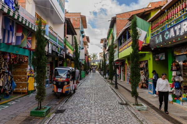 Colorful cobblestone street in Guatapé with painted shopfronts, hanging signs, souvenir stalls, and a tuk-tuk