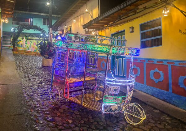 Colorful illuminated traditional transport vehicle on a cobblestone street in Guatapé, surrounded by vibrant buildings.