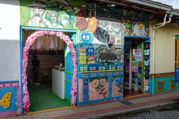 Colorful storefronts in Guatapé, Antioquia, Colombia, adorned with vibrant murals and decorations, creating a lively street scene.