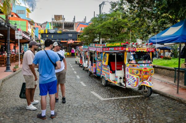 Colorfully decorated tuk-tuks parked on a cobblestone street in Guatapé with people standing nearby