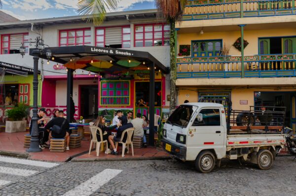 Colorful buildings line a street in Guatapé, Colombia, with a bustling outdoor café and a small truck parked nearby.