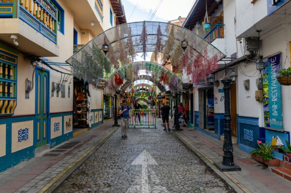 Colorful decorations hang above a cobblestone street in Guatapé, Colombia, where visitors stroll past vibrant shops and cafes.
