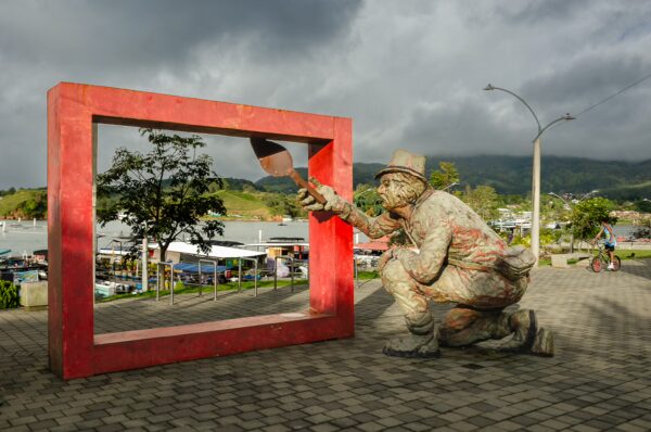 Colorful sculpture of a painter in a red frame, set against a cloudy sky in Guatapé, Antioquia, highlighting the town's vibrant culture.