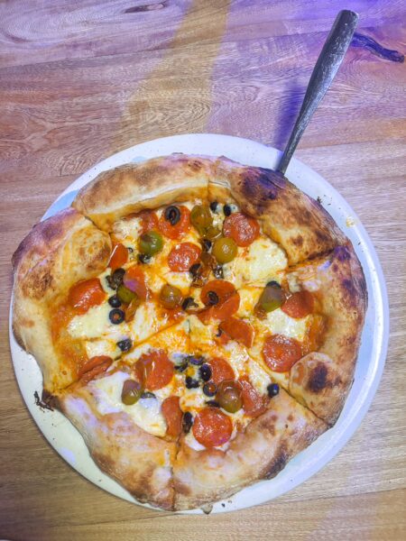 Wood-fired pizza topped with olives, pepperoni, and melted cheese on a white plate at 18once Piezzeria Napolitana, Guatapé