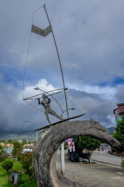 Windsurfer sculpture on a decorative wave, set against cloudy skies in Guatapé, Antioquia, showcasing the town's vibrant artistic flair.