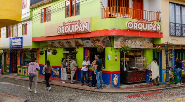 Colorful storefront of Orquipan in Guatapé, featuring vibrant green and red hues, with pedestrians enjoying the lively street scene.