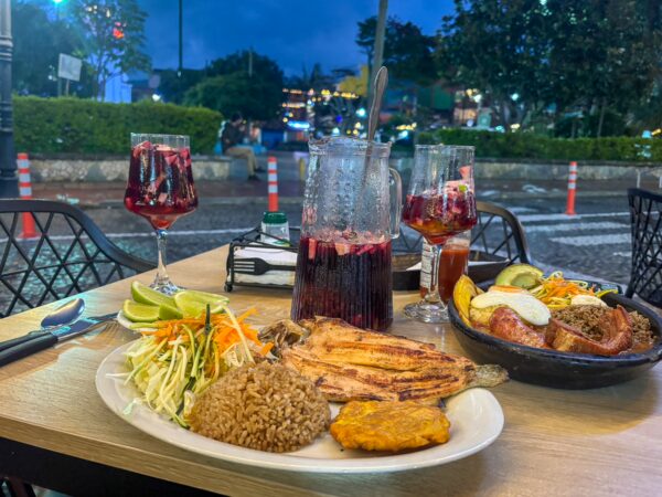 Dinner on an outdoor terrace in Guatapé with sangria, a pitcher, and Colombian plates beside the rainy square