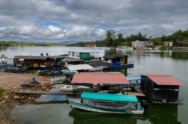Serene waters in Guatapé, Colombia, reflecting colorful boat docks and lush greenery under a cloudy sky.