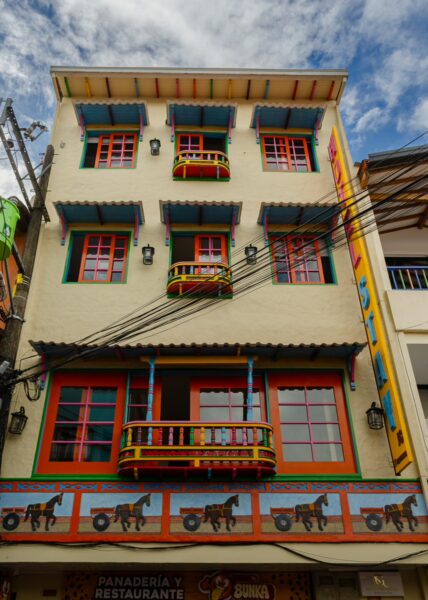 Colorful building facade in Guatapé, Antioquia, with bright windows and painted horse murals against a cloudy sky.