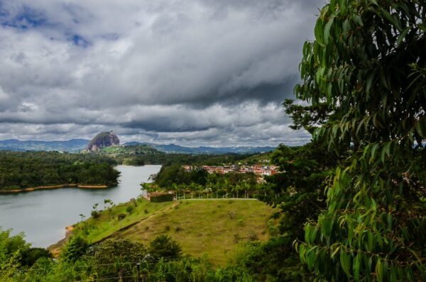 Stunning view of Guatapé's lush greenery, the lake, and El Peñol rock under a cloudy sky in Antioquia, Colombia.