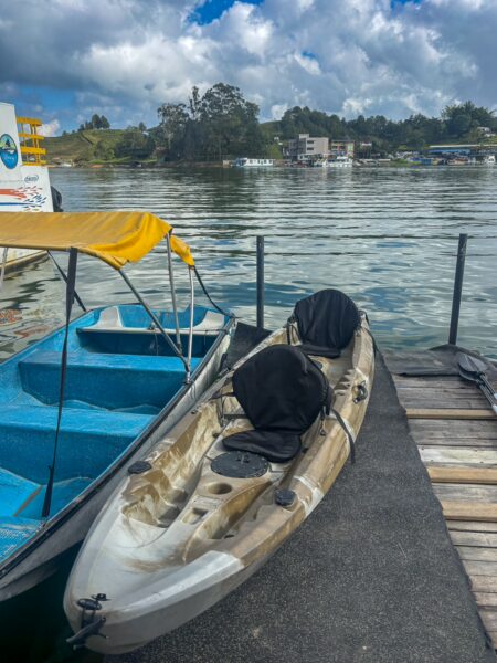 Kayaks and boats docked at a serene waterfront in Guatapé, vibrant waters reflecting the cloudy sky and surrounding greenery.