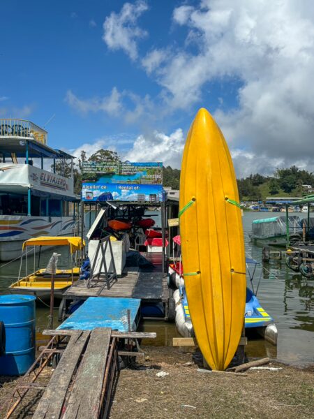 A bright yellow kayak stands at the dock in Guatapé, surrounded by colorful boats and vibrant waters under a blue sky.